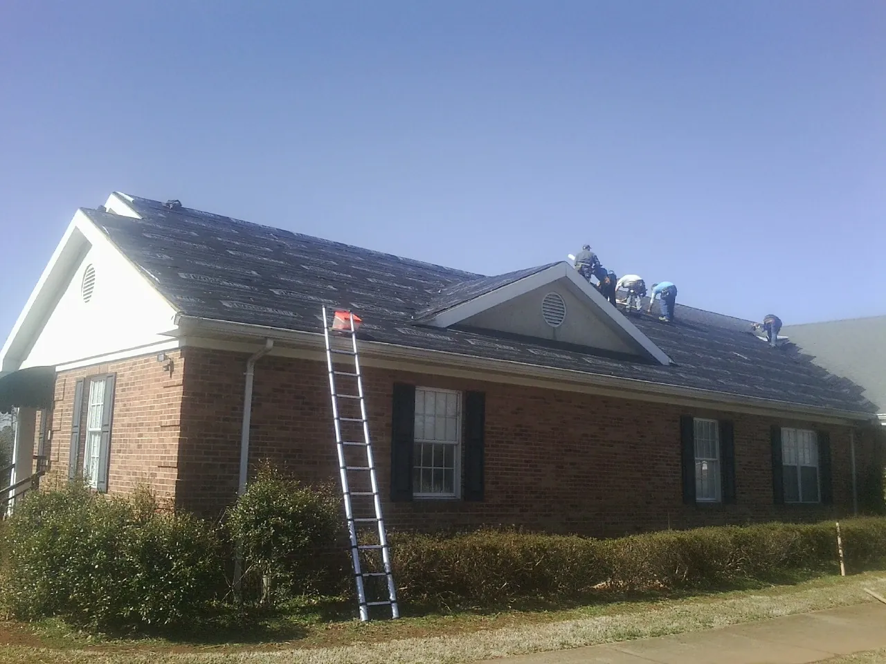 Crew tearing shingles off a brick ranch roof with a ladder set — Emergency Roof Repair work by our crew in Pocono Summit