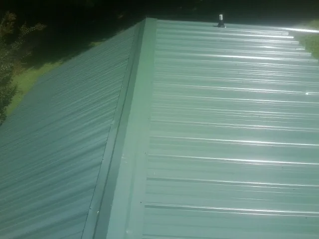 New green metal panels meeting at the ridge of a roof — Flat Roof Repair work by our crew in Pocono Summit