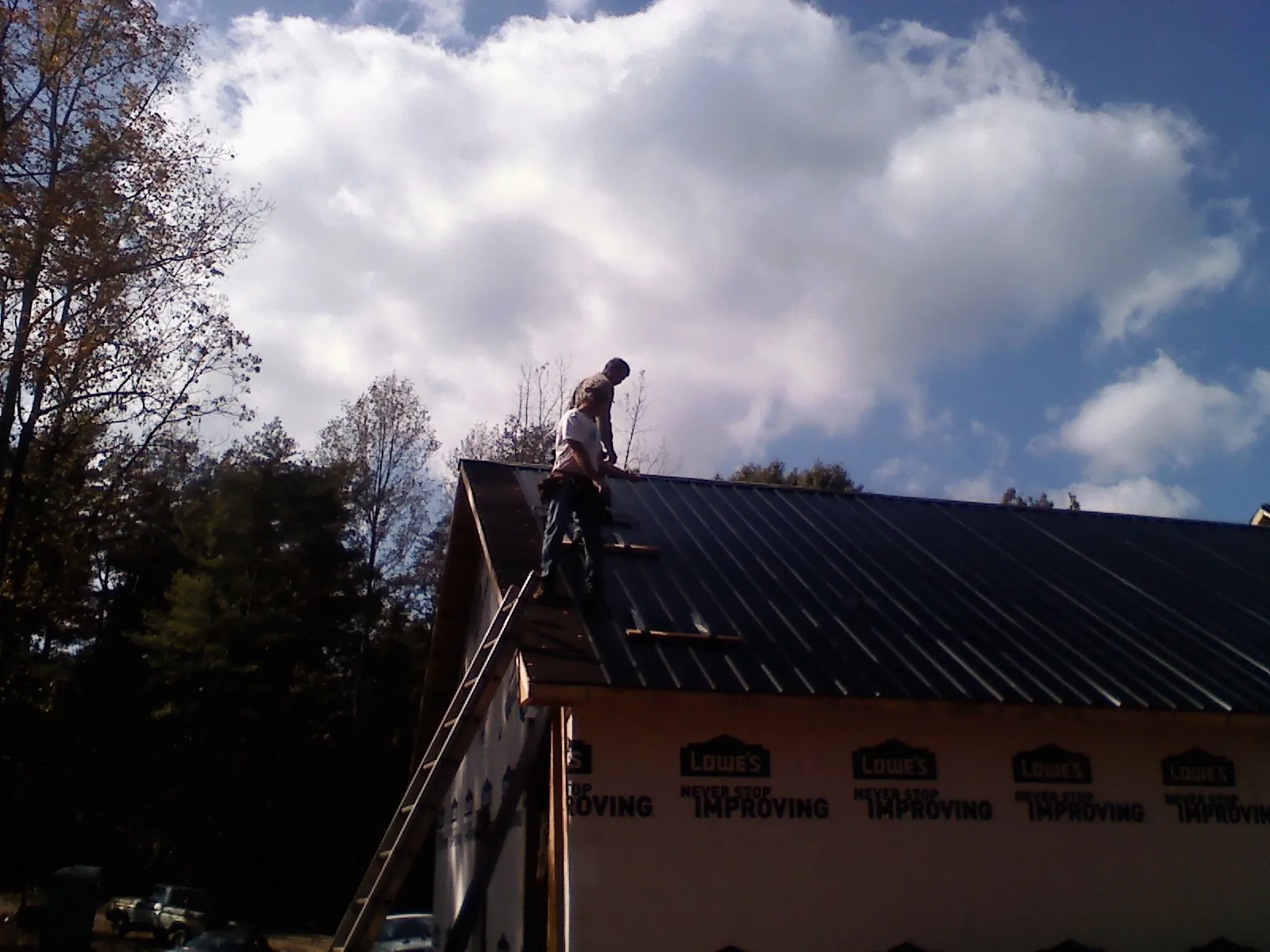 Roofer fastening dark metal panels high against a cloudy sky, from a Roof Inspection job in Pocono Summit