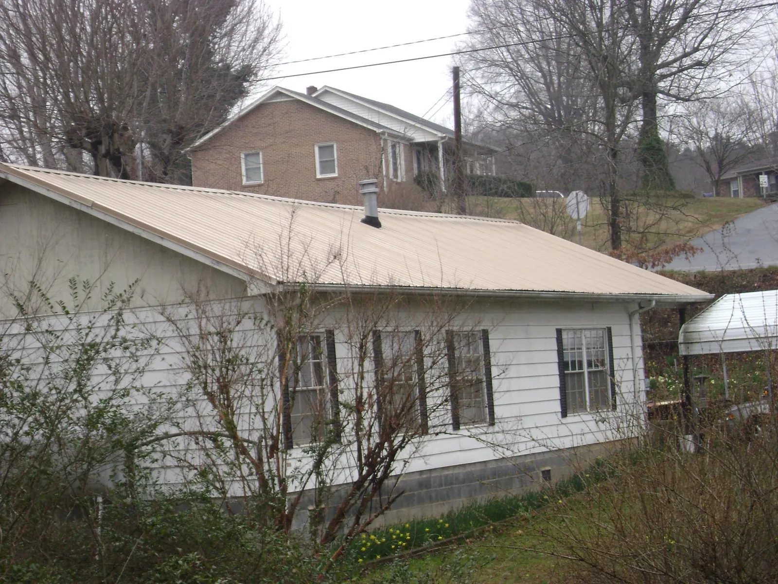 Tan metal roof on a white sided house set into a hillside — Commercial Roofing by Roofing Brothers in Pocono Summit