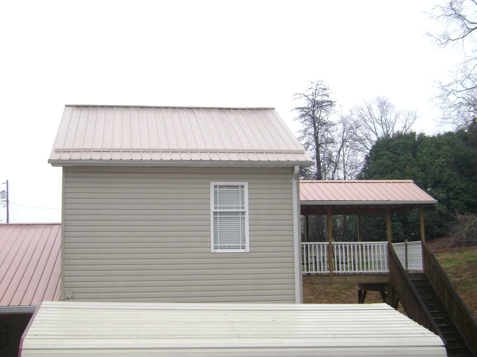 Tan metal roofs on a two story addition and attached porch, from a Roof Replacement job in Pocono Summit